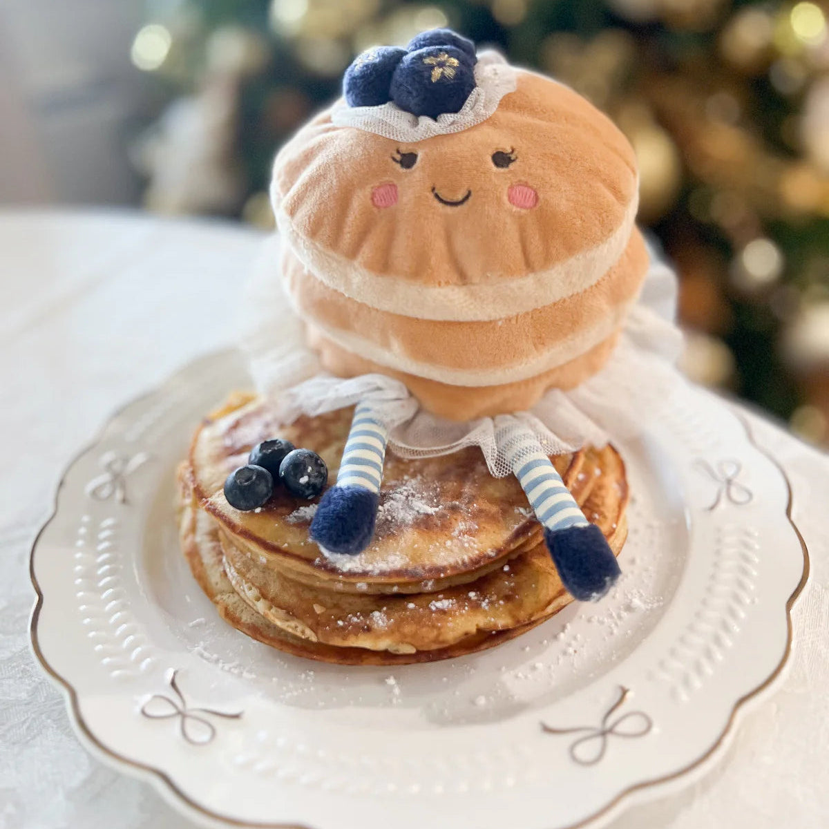 Plush toy resembling a pancake character on a stack of pancakes with a Christmas tree in the background