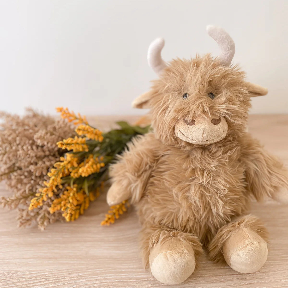 Plush toy cow with horns on a wooden surface with dried flowers