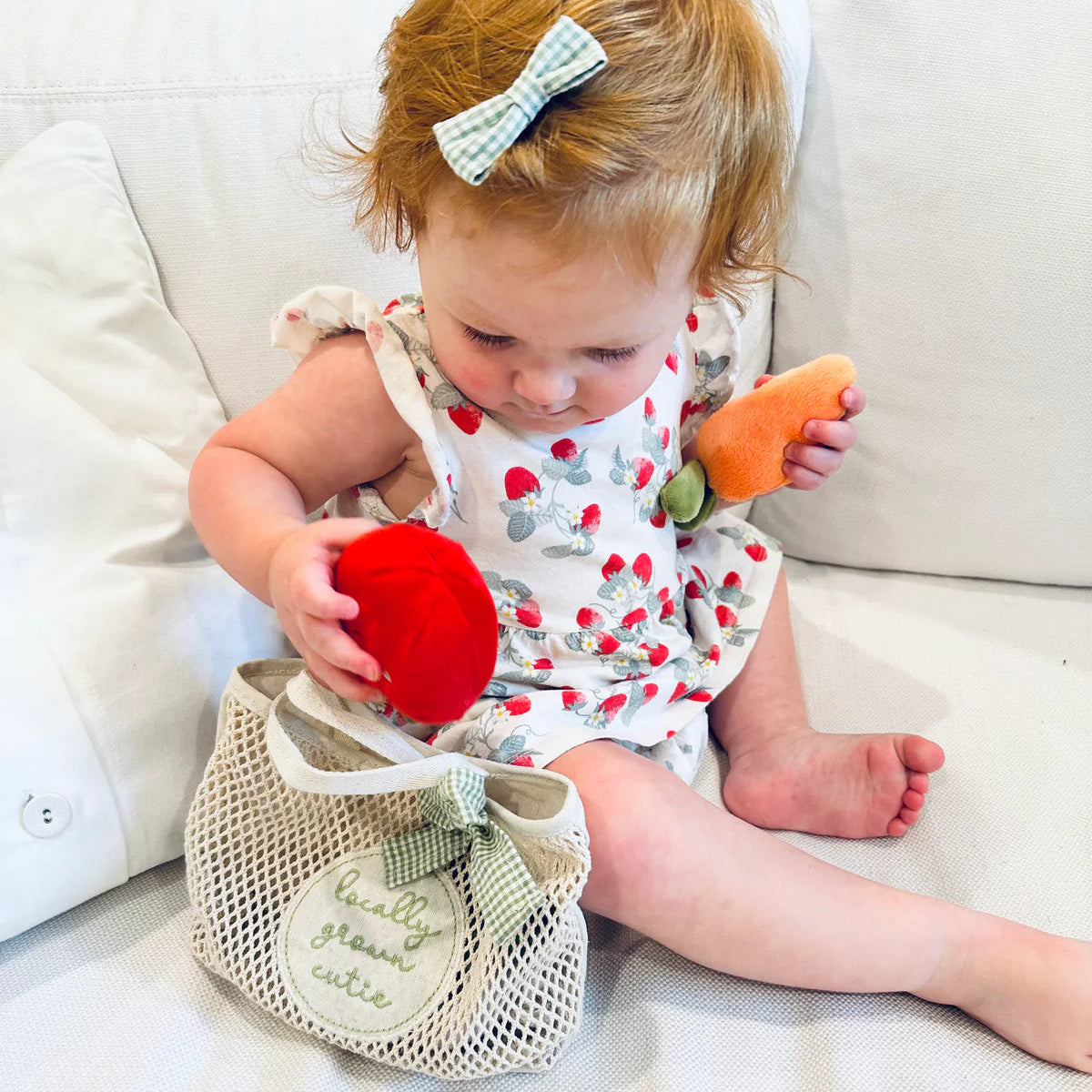 Baby playing with toy vegetables on a white couch