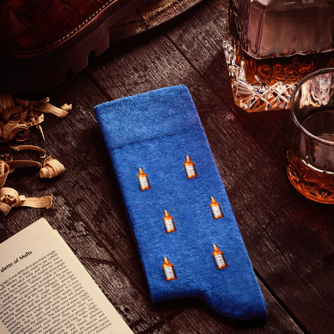 Blue phone case with bottle designs on a wooden surface with a glass of whiskey and book.