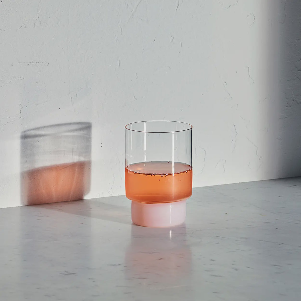 Clear glass with pink liquid on a gray surface against a light gray background