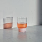 Clear glass with pink liquid on a gray surface against a light gray background