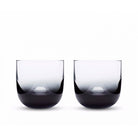 Two smokey black glass whiskey glasses with a clear upper part and black lower part, displayed against a white background.