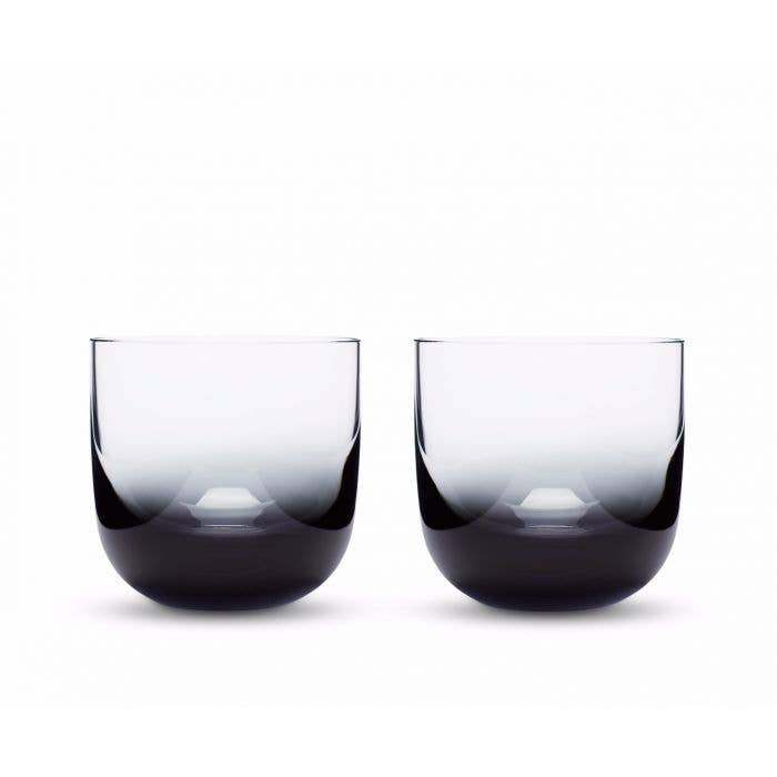 Two smokey black glass whiskey glasses with a clear upper part and black lower part, displayed against a white background.