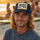 Man wearing a cap with 'Make Waves' text at sunset near water