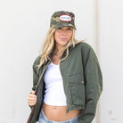 Person wearing a green jacket, white top, and light blue shorts with a camouflage cap.