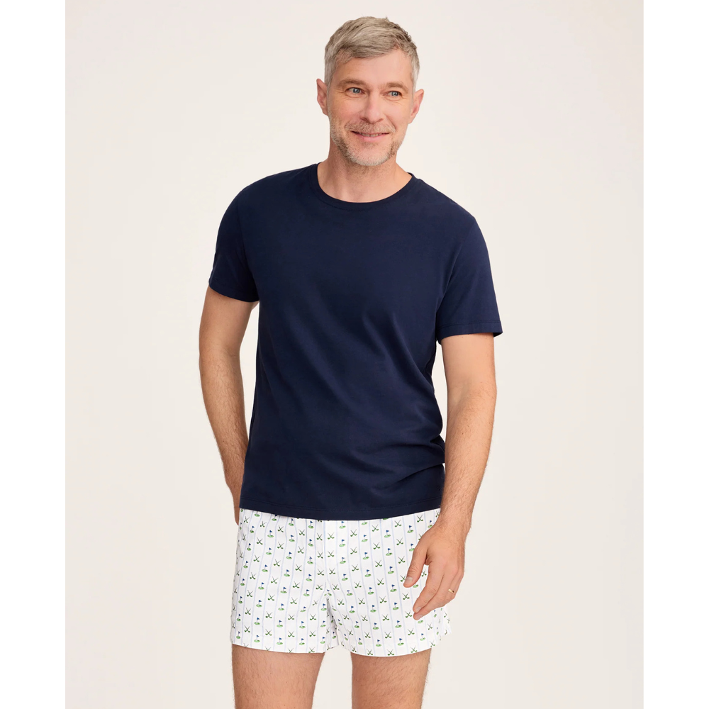 Man wearing a navy t-shirt and white patterned shorts on a beige background