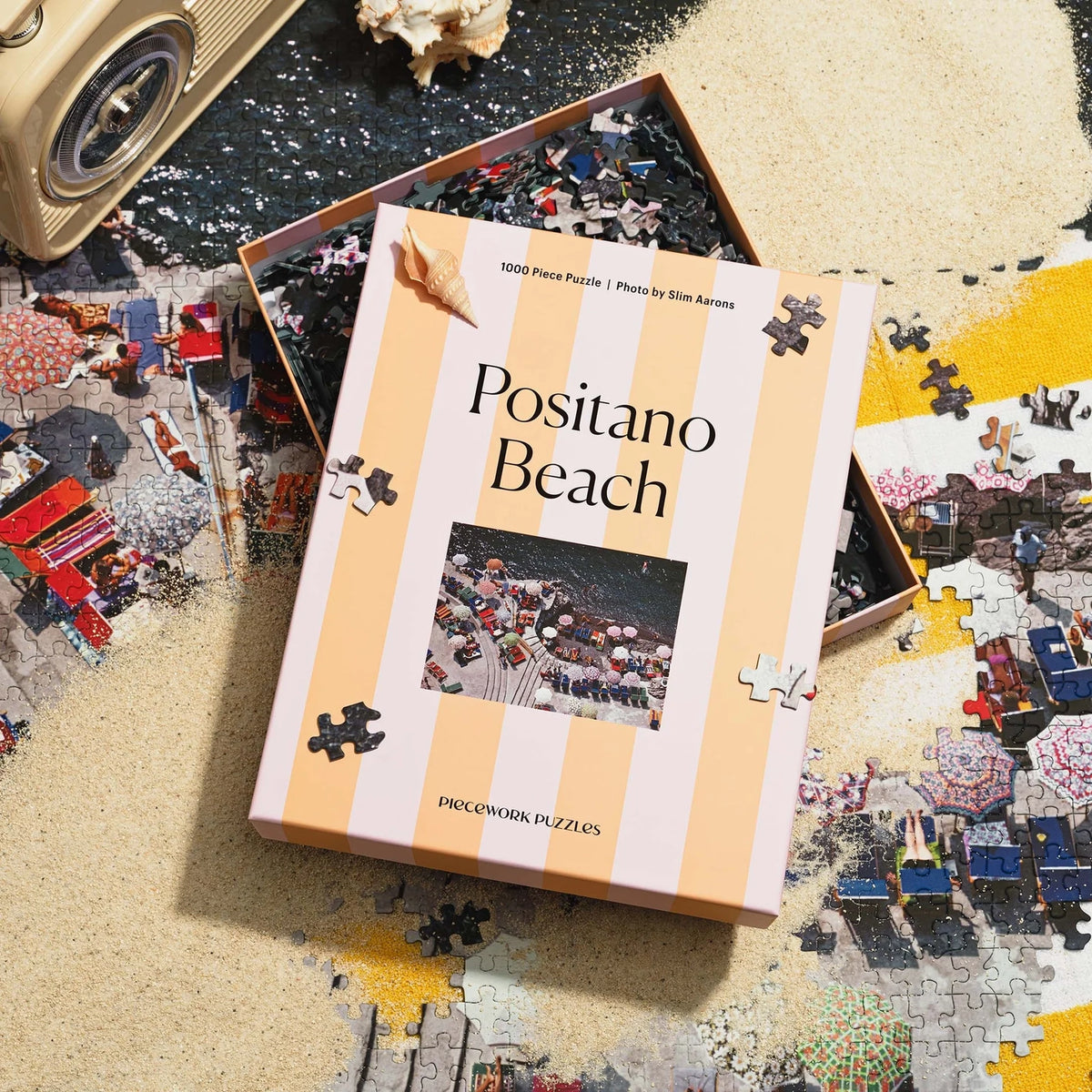 Puzzle box titled 'Positano Beach' with a partially completed puzzle on a sandy surface.