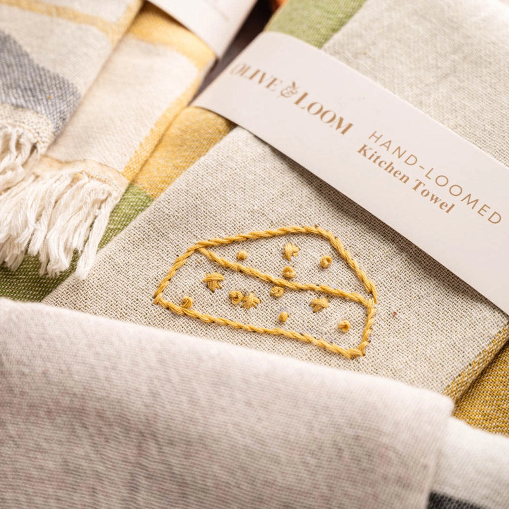 Hand loomed kitchen towel with embroidery and brand label on a matching fabric background
