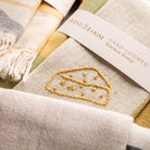 Hand loomed kitchen towel with embroidery and brand label on a matching fabric background