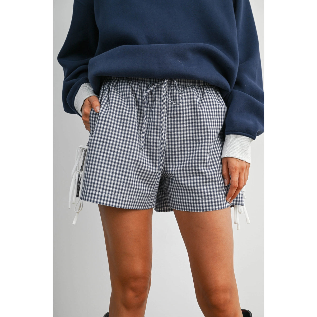 Person wearing navy sweatshirt and checkered shorts on a plain background