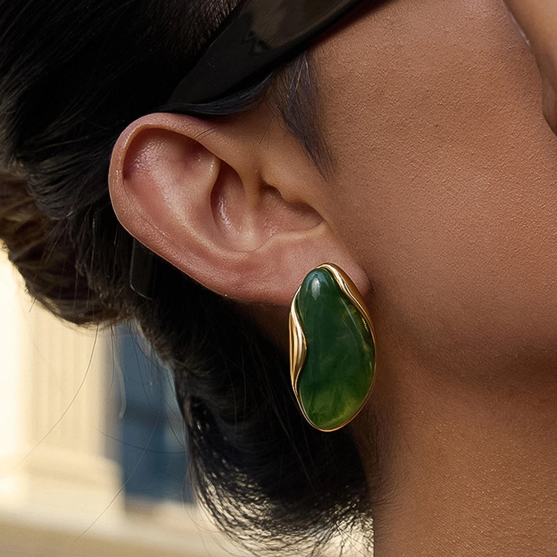 Close-up of a person wearing a green earring with a gold setting.