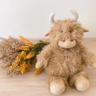 Plush toy cow with horns on a wooden surface with dried flowers