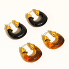 Set of four hoop earrings in black, gold, and amber colors on a white background