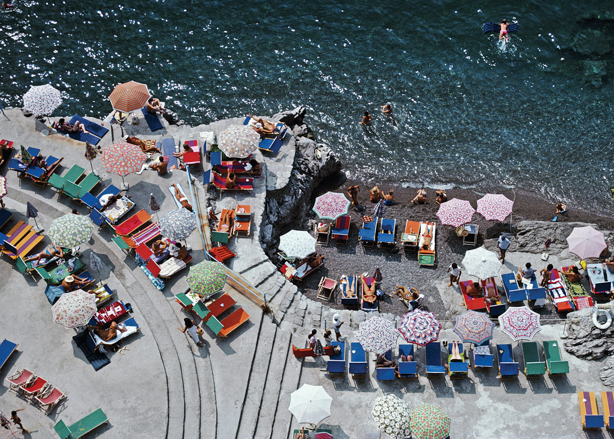 Outdoor seating area with colorful chairs and umbrellas by a waterfront.