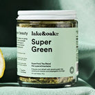 Jar of 'Super Green' tea blend with 'lake&oak tea co.' label on a green surface.