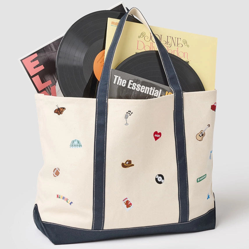 Beige tote bag with black trim holding vinyl records on a light gray background