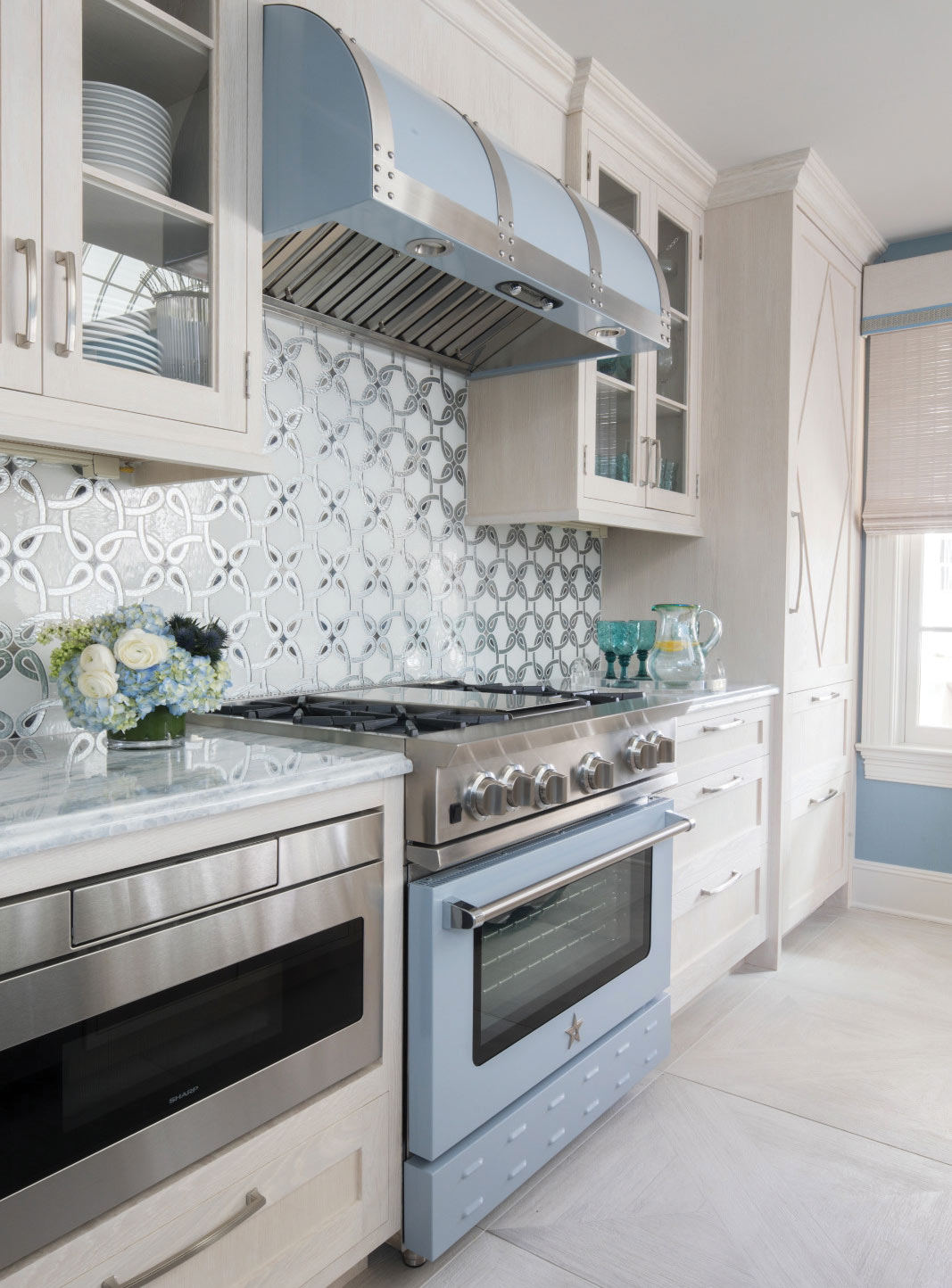 A custom BlueStar stove and hood are set against a luxe geometric glass backsplash and white iceberg quartzite countertops. 