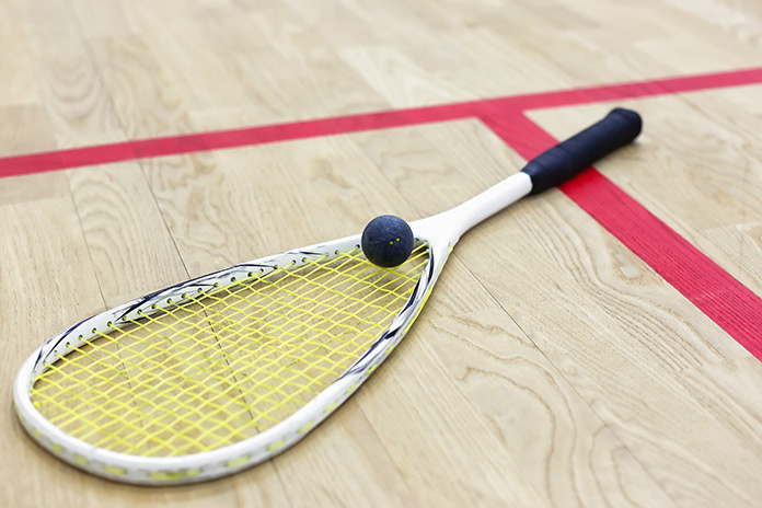 A squash racquet on the floor of a court with a ball on top.